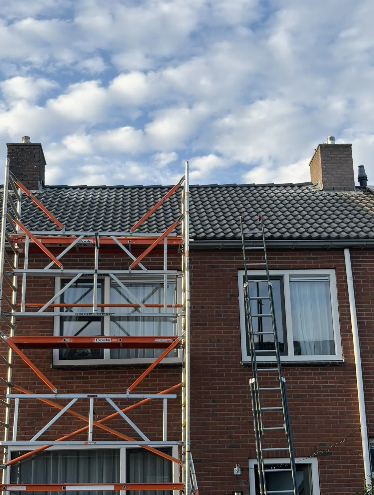 Rijwoning met nieuw pannendak en schoorstenen, rolsteiger aan de gevel